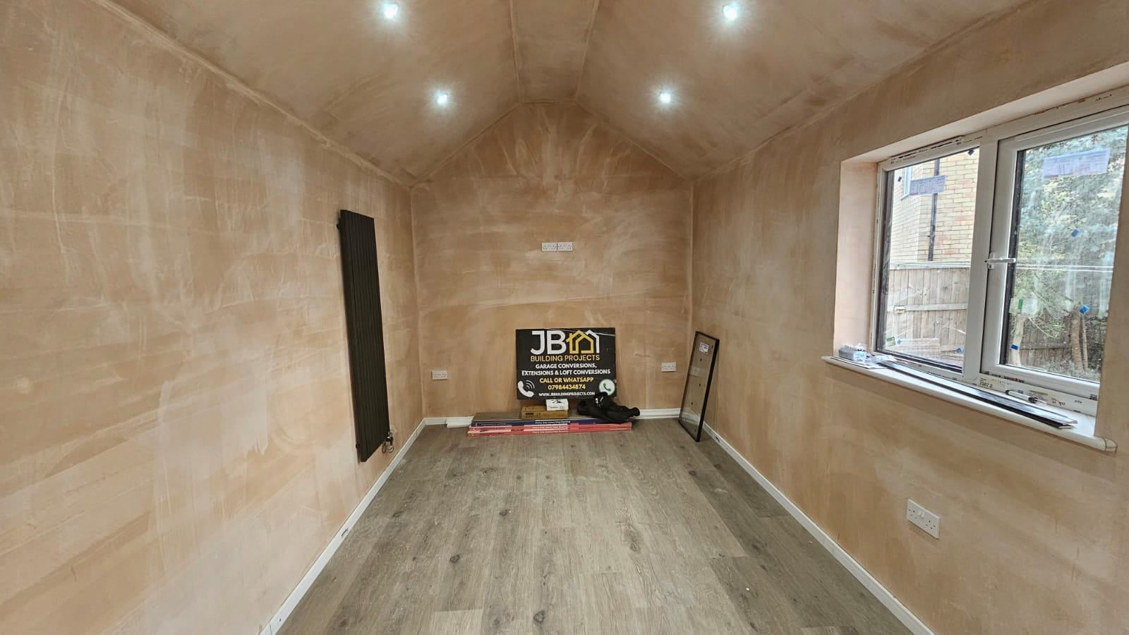 Dunmow garage office before decoration, with a vaulted plaster ceiling, recessed downlights, wood-effect flooring and a vertical radiator
