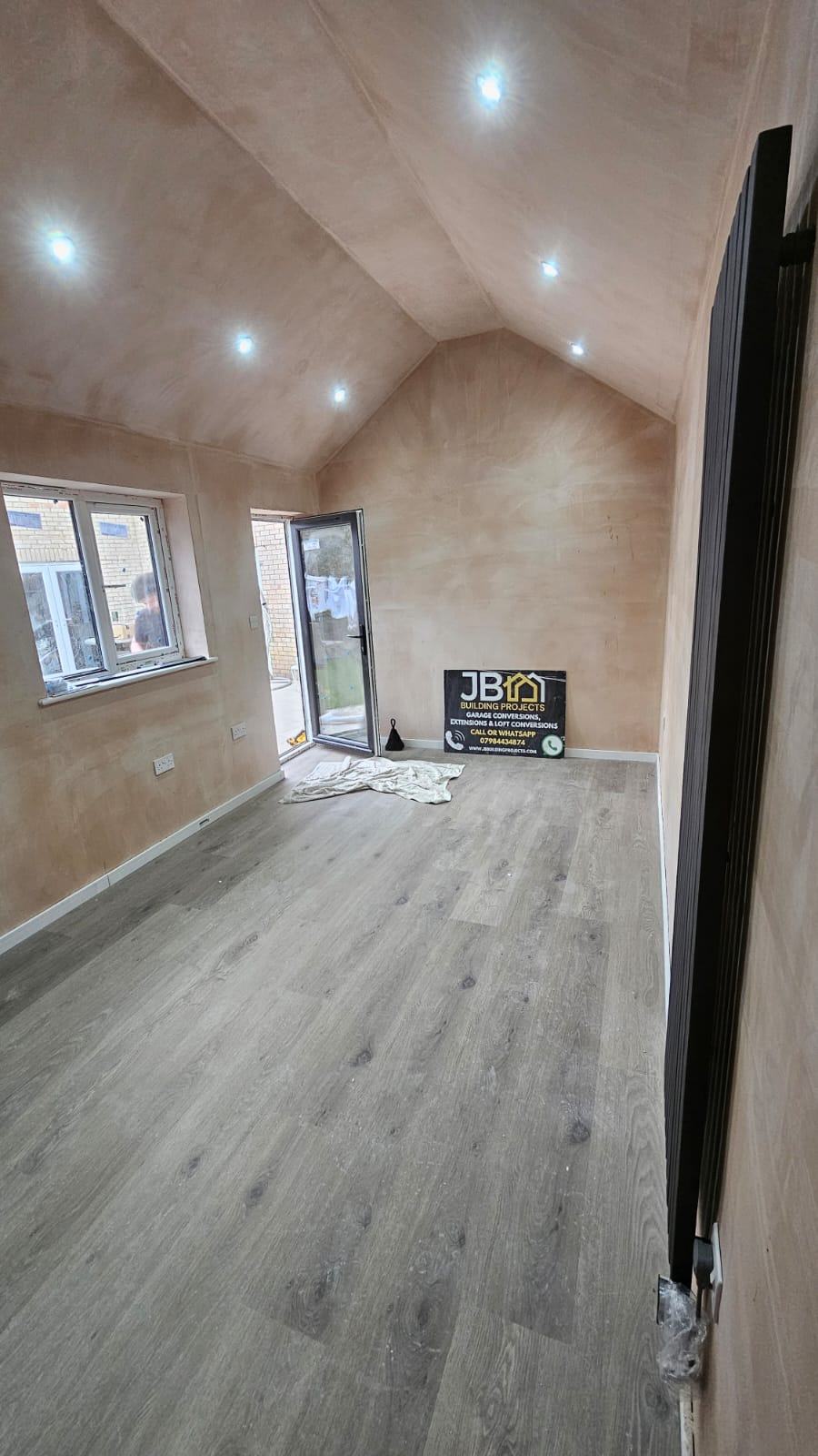 Reverse view of the Dunmow office before decoration, showing wood-effect flooring, downlights, window, glazed door and vertical radiator