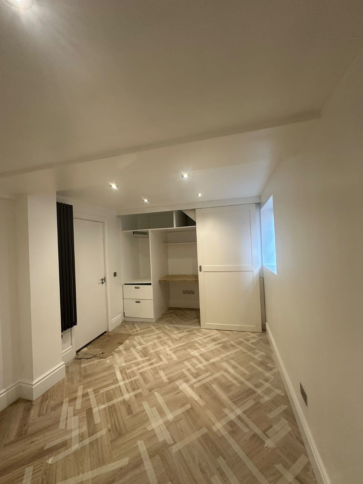 Completed Waltham Cross garage office with white bespoke sliding-panel units, an integrated desk, recessed downlights and herringbone flooring