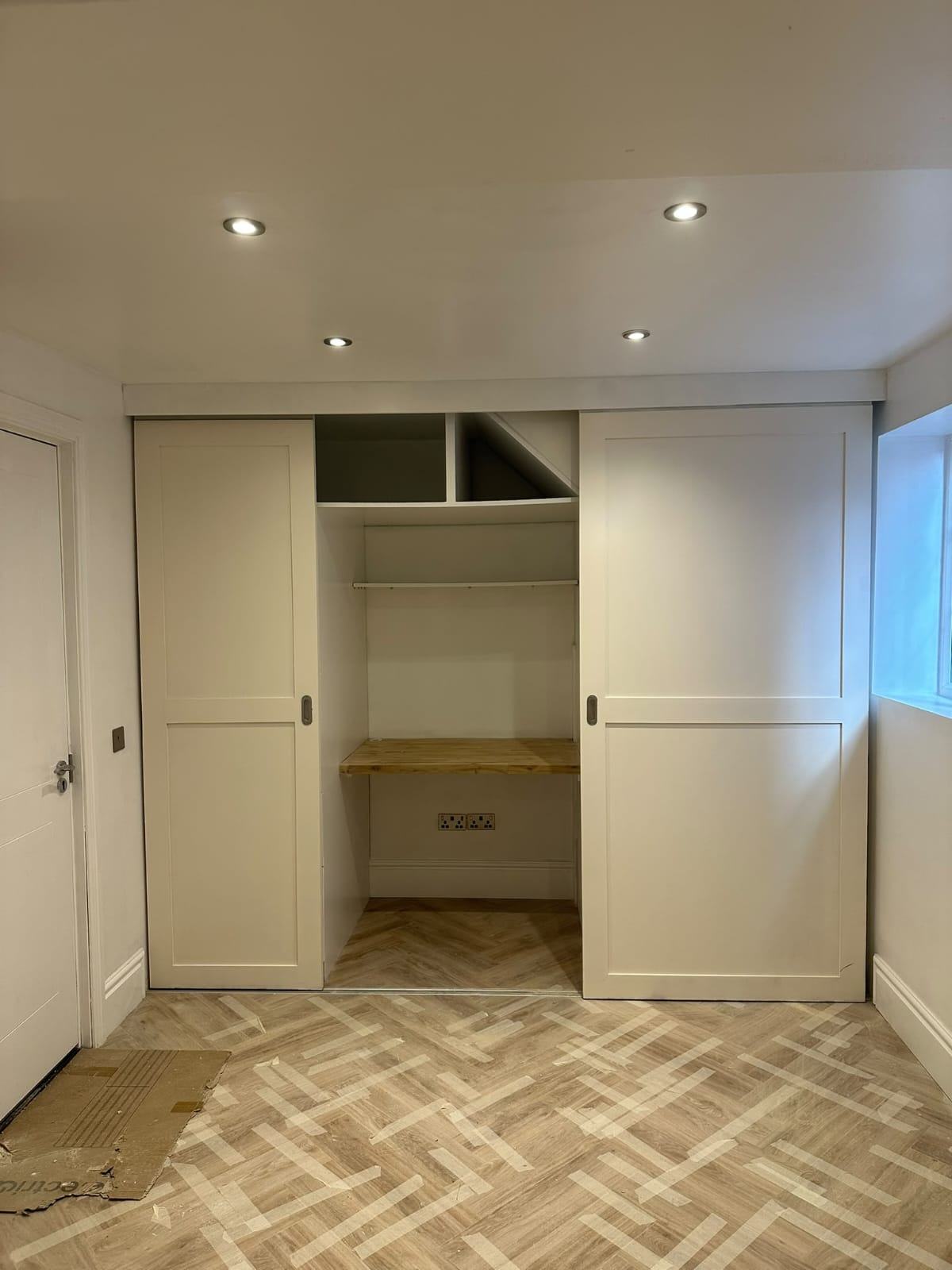 White bespoke carpentry units in the Waltham Cross office with a central timber worktop, open upper cubbies and sliding panel doors
