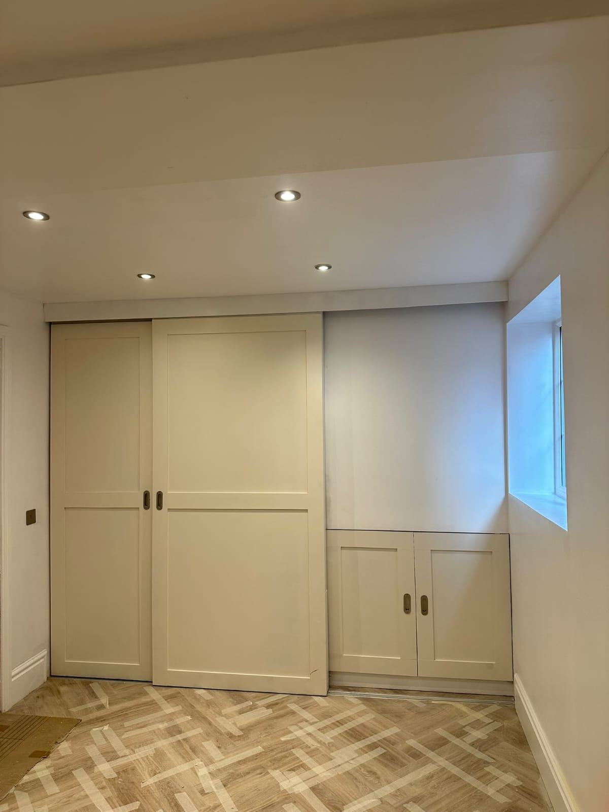 The finished white sliding-front carpentry units with the doors closed above the office herringbone floor